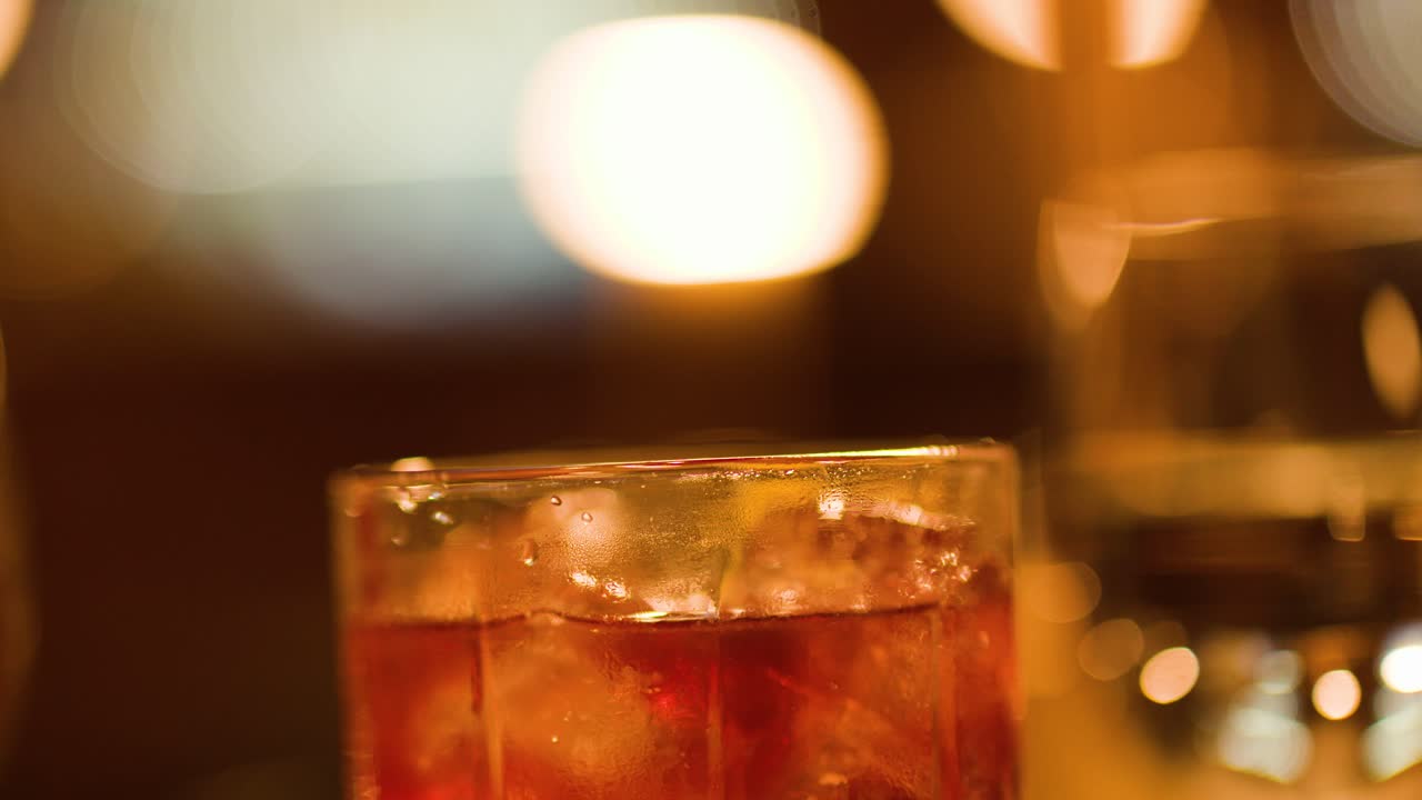 Primo piano di un cocktail con ghiaccio su un bancone bar, illuminazione ambrata, profondità di campo ridotta, atmosfera serale