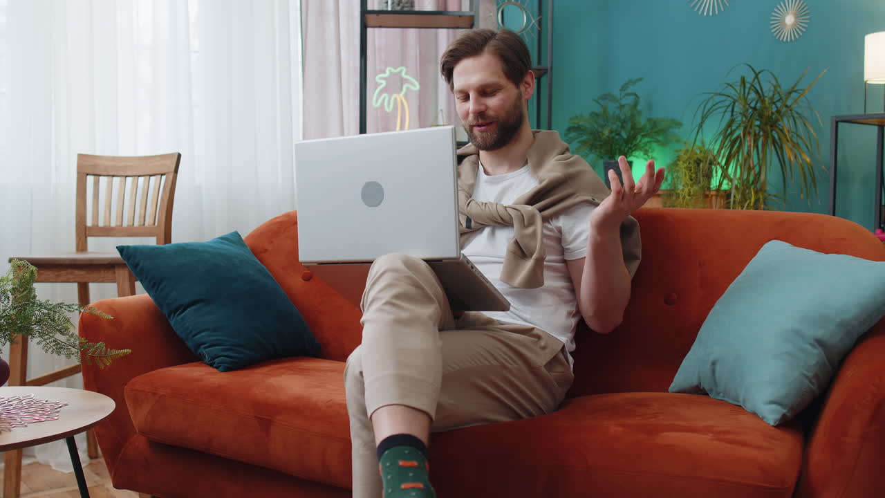 Man sitting on home couch looking at camera making video conference call with friends or family