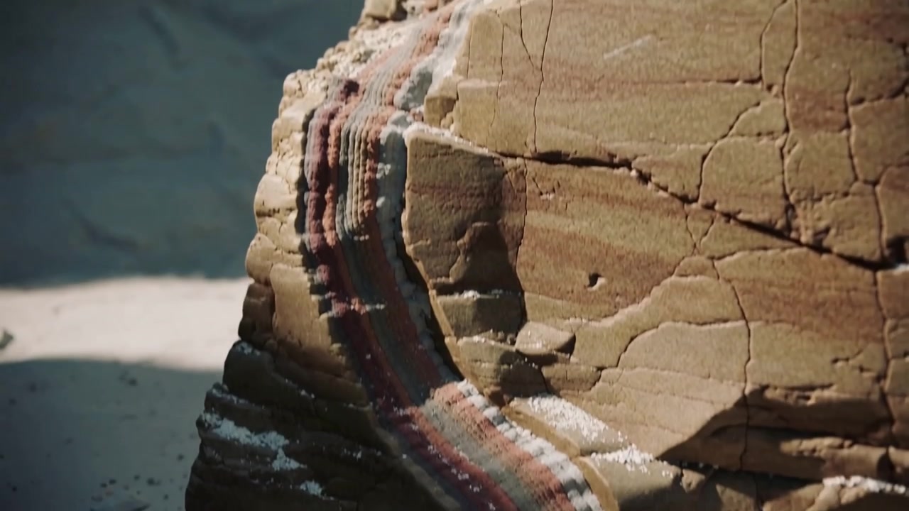 Telecamera in panoramica che rivela roccia erosa sulla sabbia, esponendo una fascia di colore e sale per mostrare l'intera banda.