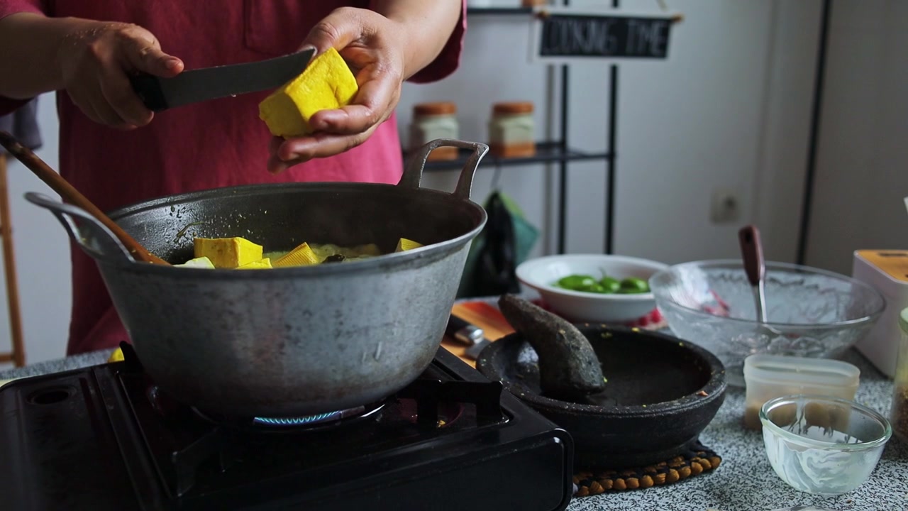 Cozinheiro caseiro fatiando tofu amarelo fresco diretamente em panela de curry fervente no fogão a gás.