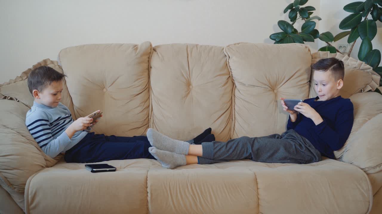 Preschool boys holds modern mobile phone and plays cheerfully video game. Focus on smartphone.