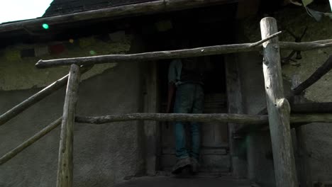 mochilero masculino milenario subiendo escaleras de casa rural al aire libre, destello de lente de luz solar