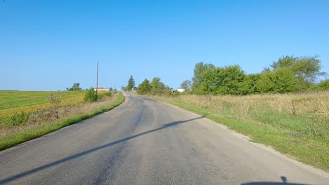 POV-driving-on-rural-county-road-with-no-center-line-past-maturing-fields,-farmyards,-and-grain-storage-bins-in-rural-Iowa-on-a-sunny-early-autumn-day