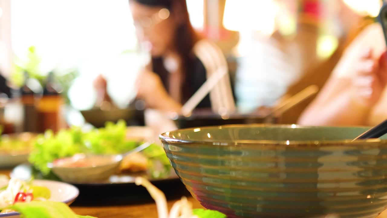 Chopsticks lift noodles from a pho bowl in a vibrant Bangkok restaurant, capturing the essence of Vietnamese cuisine