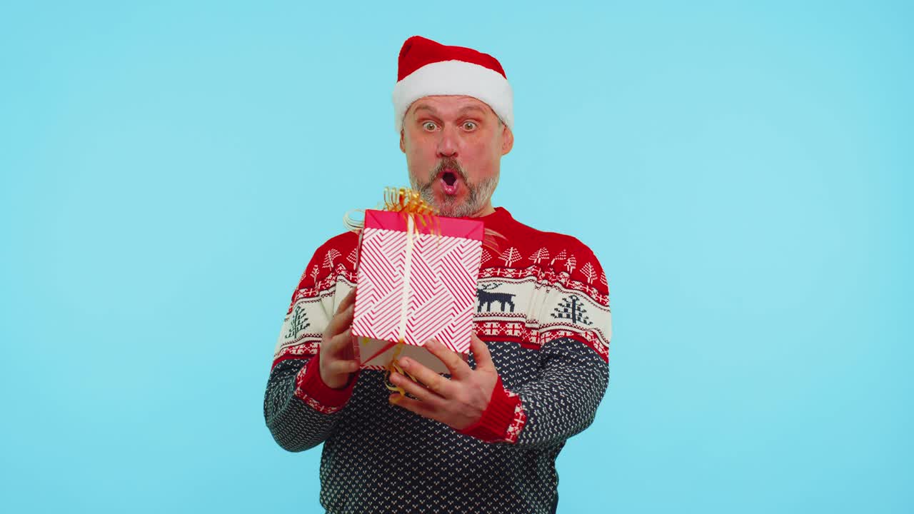 스웨터를 입은 쾌활한 남자 산타 크리스마스 모자 선물 상자, 놀라움 행복을 표현