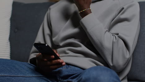 close up of man wearing hoodie sitting on sofa at home messaging or browsing on mobile phone