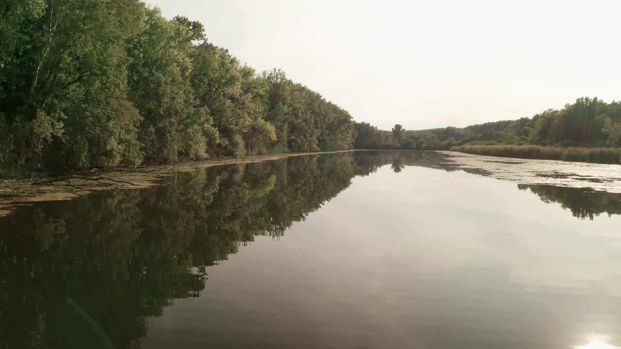 пролетая низко над небольшим спокойным озером, окруженным деревьями, в конце летнего дня