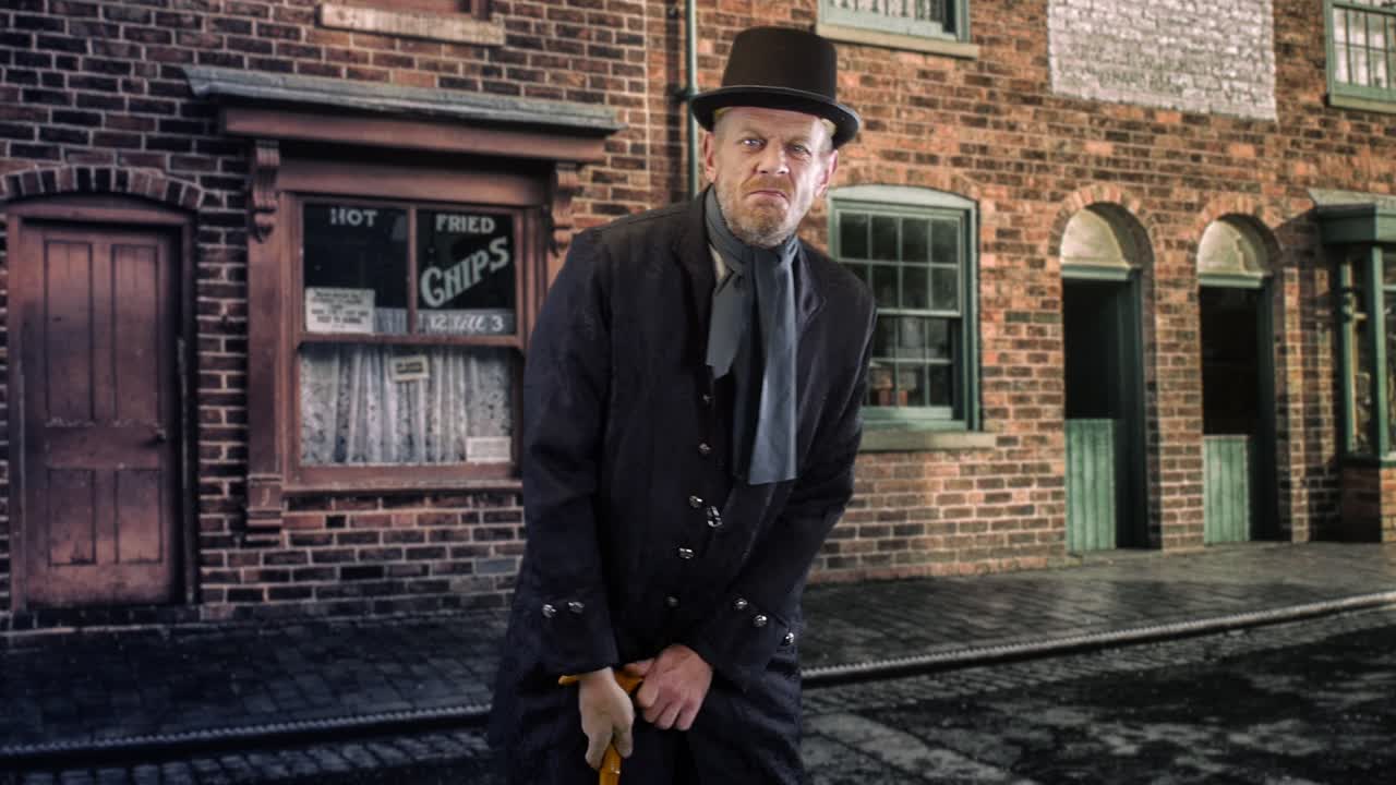 에베니저 스크루지는 빅토리아 시대 거리에 서서 화를 내며 지팡이를 흔들고 있습니다.