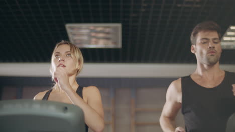 concentrated couple running together on treadmill machine in gym club.