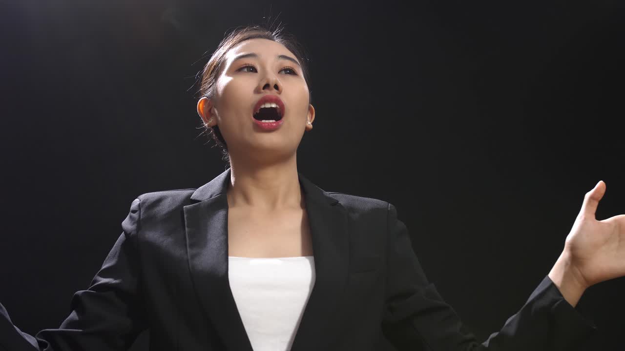 블랙 스크린 스튜디오 에서 연설 하는 동안 손 을 고 있는 비즈니스 슈트 를 입은 아시아어 연설자 여자 의 근접 사진
