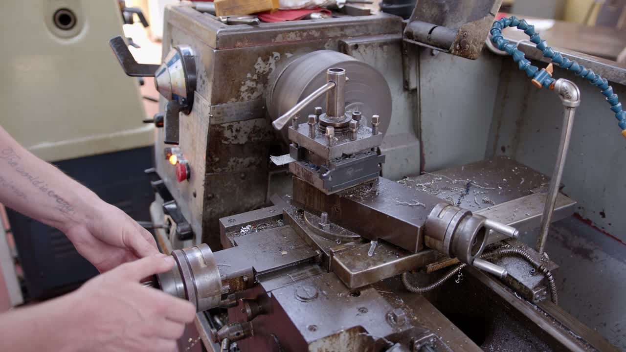 An engineer turns a handle as he shaves metal from a larger metal bar on a metal turning lathe