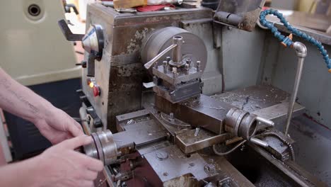 un ingeniero gira un mango mientras afeita el metal de una barra de metal más grande en un torno de torneado de metal