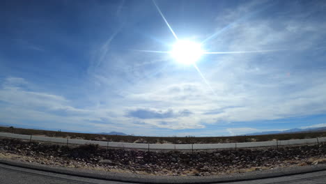 traveling along a mojave desert highway with a bright sun overhead and joshua trees marking the arid landscape