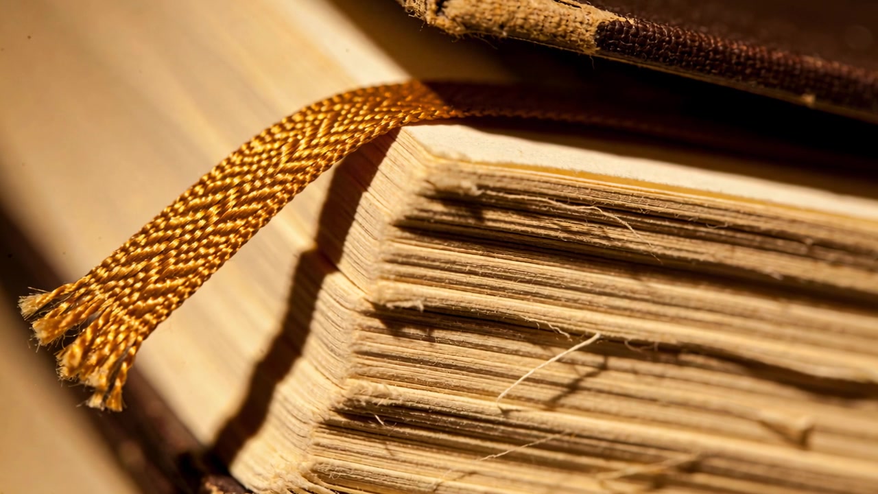 Luce calda cangiante rivela un libro rilegato in tela su una scrivania, mostrando il blocco di pagine con bordi sfrangiati e un nastro dorato.