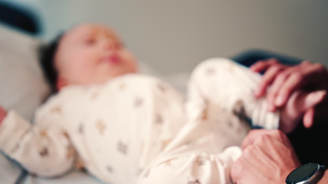Adult hand gently rests on a baby's torso while the infant lies on a padded surface