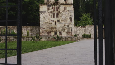 Paved-walkway-and-bell-tower-behind-open-iron-gate,-Mtsvane-monastery