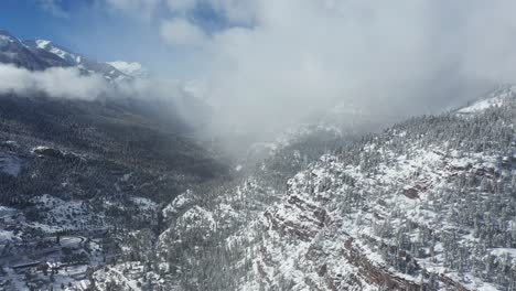 Vista-Aérea-De-Las-Nubes-Sobre-Las-Colinas-Cubiertas-De-Nieve-Blanca-Y-Ouray,-Pequeña-Ciudad-Del-Valle-En-El-Suroeste-De-Colorado,-Ee.uu.-En-El-Soleado-Día-De-Invierno,-Disparo-De-Drones