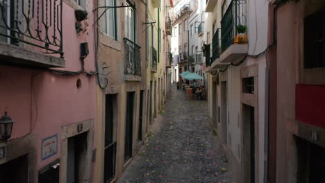 Point-of-view-street-view-of-walking-on-the-cobblestone-streets-in-Lisbon,-Portugal-with-people-sitting-and-chatting-in-local-cafes