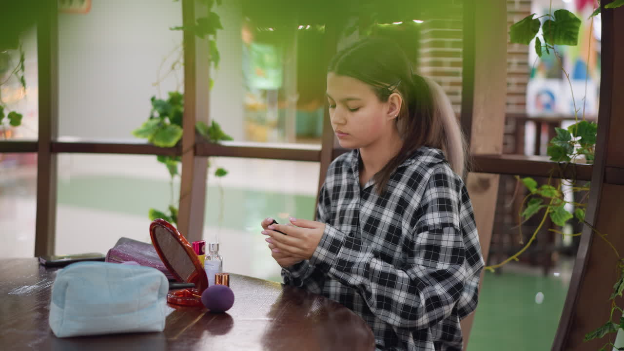 joven aplicando cuidadosamente el maquillaje mientras se mira en el espejo en la mesa de madera, herramientas de belleza, botella de suero y accesorios de maquillaje esparcidos en un fondo suavemente borroso con plantas verdes