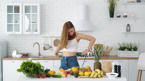 Young athletic girl measures her waist near a table with healthy food. Fruits and vegetables for diet and weight loss