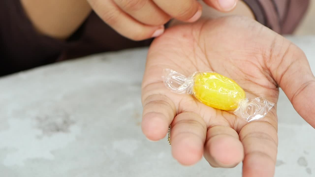 mano con un caramelo amarillo envuelto