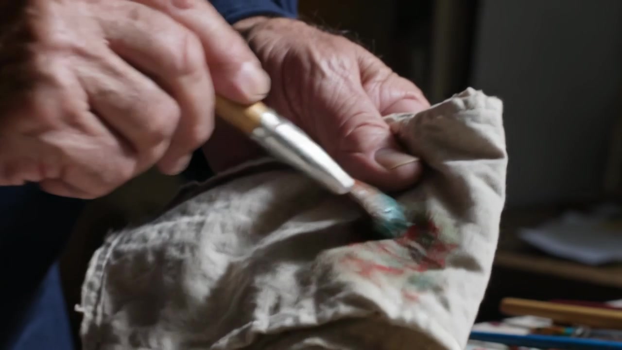 Pressing brush with green-red paint, hands wearing blue shirt wiping rag in studio, removing paint