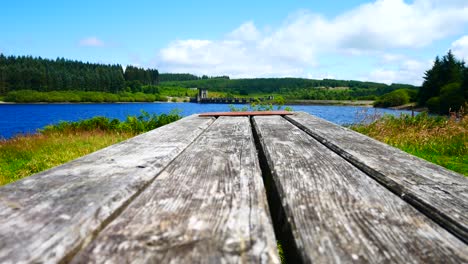 low angle wooden plank picnic table overlooking blue sky scenic reservoir lake landscape dolly right