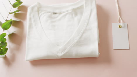 video de primer plano de una camiseta plegada blanca con etiqueta en fondo rosa