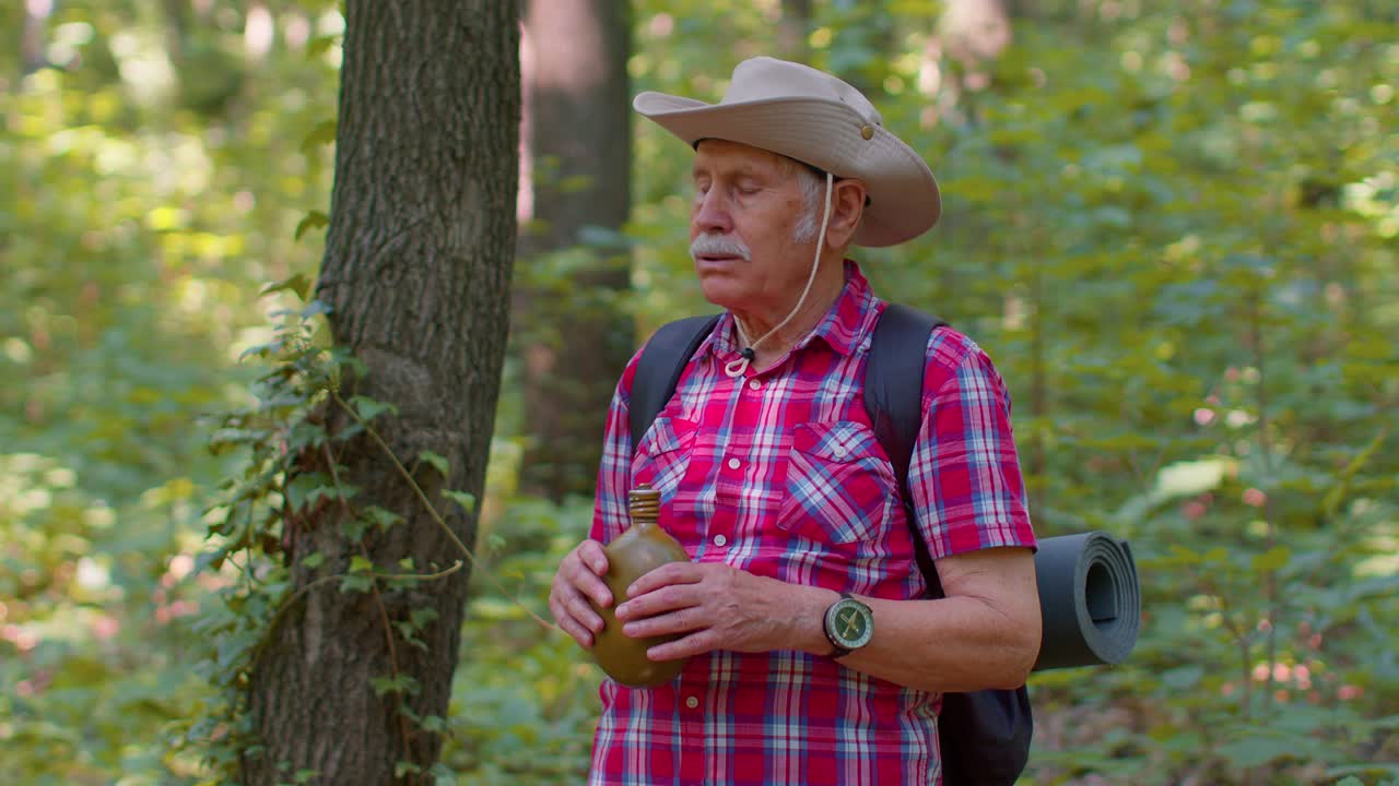 cansado sediento senior viejo excursionista caucásico abuelo relajándose, bebiendo agua en el bosque después de caminar