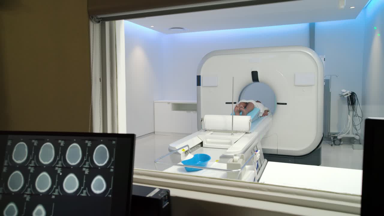 Dopo i controlli, due membri dello staff posizionano il paziente, poi spingono il lettino nel gantry per una scansione della testa.