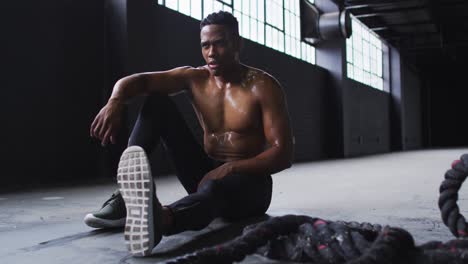 shirtless african american man resting after battling ropes in an empty urban building