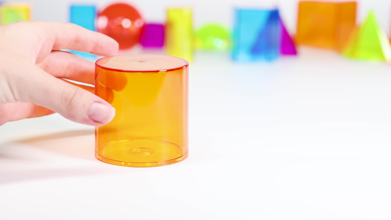 A hand interacts with vibrant 3D geometric shapes on a white surface, illustrating basic mathematical concepts in a playful setting