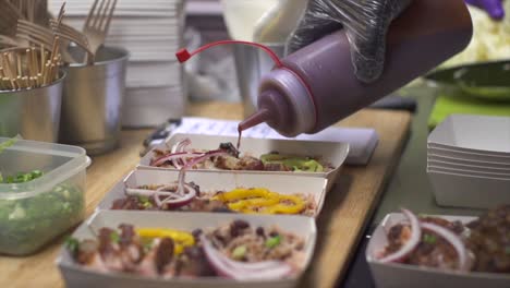 Tomato-barbecue-sauce-being-squeezed-out-of-bottle-onto-container-of-freshly-grilled-meat-and-vegetables,-filmed-in-slow-motion