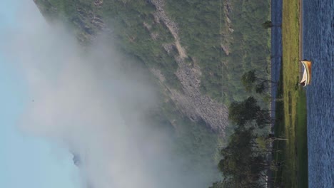 Vertical---Barco-Vacío-Flotando-En-El-Lago-Olaheimvatnet-Contra-La-Montaña-Detrás-De-Las-Nubes-En-Noruega