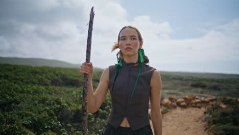 beautiful girl trekking path holding stick. solo traveler exploring wild terrain