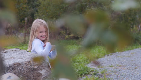 Handheld-Porträt-Eines-Blonden-Skandinavischen-Kleinen-Mädchens,-Das-Sich-Im-Freien-An-Einen-Felsen-Lehnt