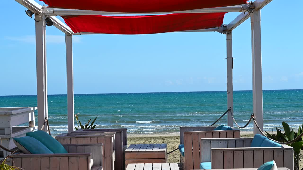 A seaside lounge shaded by a striking red canopy, overlooking the Mediterranean Sea in Larnaca, Cyprus