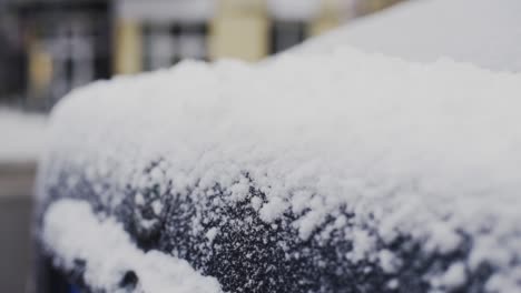 Thin-layer-of-fresh-white-snow-covering-black-car-trunk-in-winter,-close-up