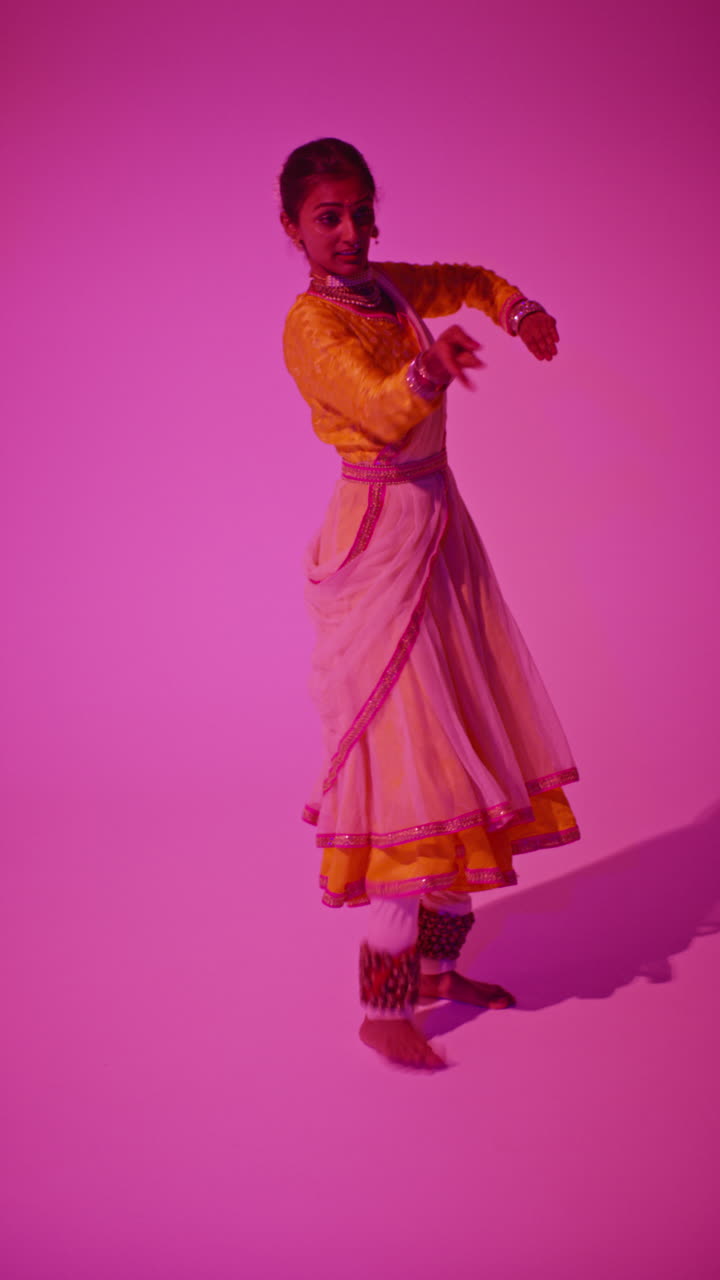 video vertical de larga duración en estudio de una bailarina de kathak que realiza un baile vestida con el vestido tradicional indio contra un fondo púrpura 5