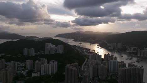 Urban-coastal-scenery-with-suspension-bridge-and-high-rise-buildings-during-golden-hour,-facing-the-sun