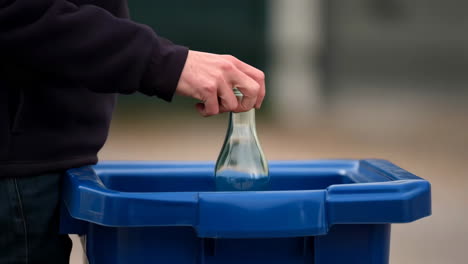 a person recycles glass bottles into a blue recycling bin