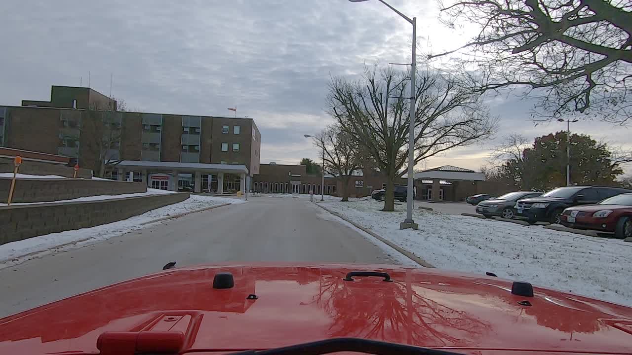 POV driving on quiet road toward a rural hospital with an Emergency Room on a snowy afternoon; Point of View through the windshield of a red vehicle