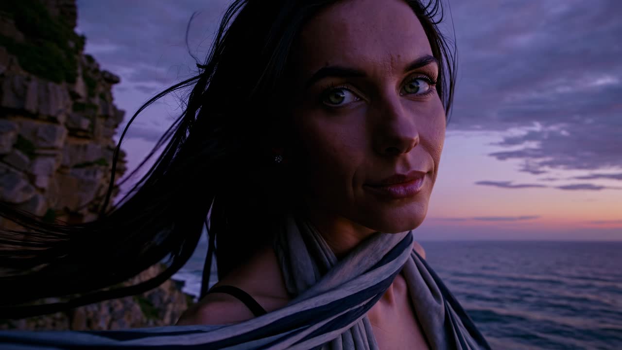 Close-up video shot of a woman by the sea at sunset, capturing a contemplative mood with a low-angle