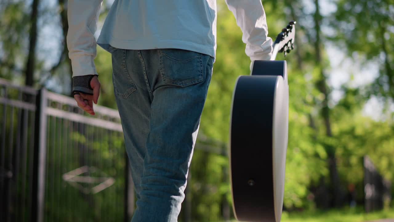 solo guitarist walking with guitar case, closeup rear view along treelined path, casual jeans and long sleeve shirt, slow rhythmic sway of case, warm spring light and soft bokeh, reflective mood