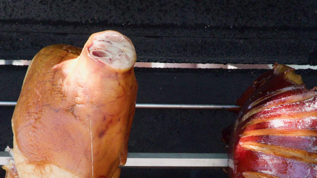 Juicy pork knuckles slowly rotate on a spit above open flames, close-up, natural lighting