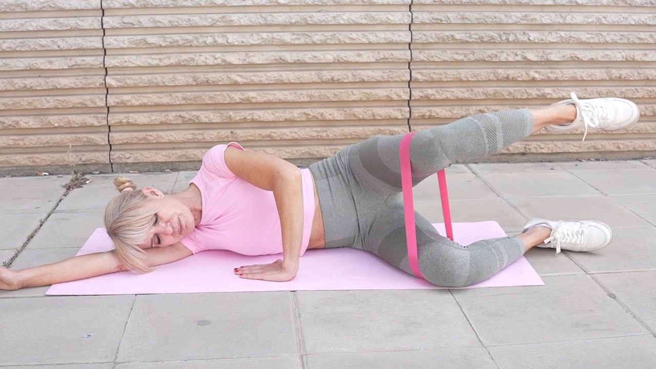 Woman doing side leg raise with resistance band outdoors for flexibility and endurance