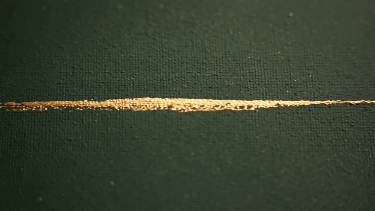 Reagendo alla perla destra, una pennellata oro metallizzato che si espande e si ispessisce su una tela verde scuro texturizzata