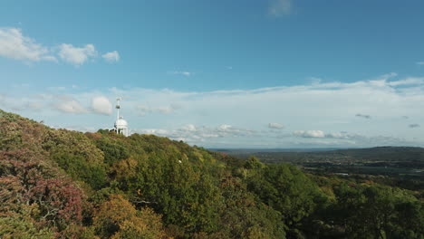 flight above fall forest on mountain with water tank and telecom tower atop