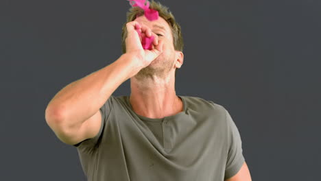 man blowing pink confetti on grey screen