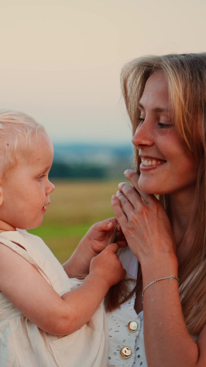 Junge Mutter hält ihre Kleinkindtochter bei Sonnenuntergang auf einem Feld